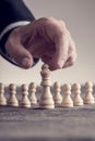 Human hand wearing suit reaching white queen chess piece at table