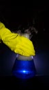 A human hand wearing yellow rubber glove holding Erlenmeyer flask with a blue liquid inside on a dark background Royalty Free Stock Photo