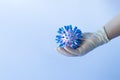 A human hand in a white medical glove holds a mock-up of a blue coronavirus molecule. Close-up