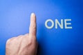 Human hand beside the word One written with plastic letters on blue paper background Royalty Free Stock Photo