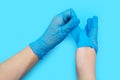 Human hands in blue surgical gloves with a gesture remove gloves, on blue background with close-up.