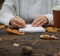 Human hands with a cup of coffee and scarf at wooden table with notebook and pen and autumn leaves. Human hands with a cup of Royalty Free Stock Photo