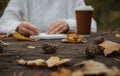 Human hands with a cup of coffee and scarf at wooden table with notebook and pen and autumn leaves. Human hands with a cup of Royalty Free Stock Photo