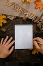 Human hands with a cup of coffee and scarf at wooden table with notebook and pen and autumn leaves. Human hands with a cup of Royalty Free Stock Photo