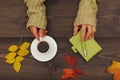 Human hands with a cup of coffee at a wooden table with notebook and pen and autumn leaves Royalty Free Stock Photo