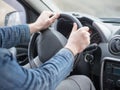 Human arms in denim sleeves on steering wheel, inside cab view, close up, selective focus. Ordinary man driving a car.