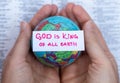 Human hands hold handwritten verse quote, God is King of all earth upon world globe and open Holy Bible Book Royalty Free Stock Photo