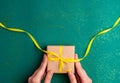 Human hands holding brown gift box with a yellow satin ribbon bow on emerald green background with gold colored glitter. Christmas Royalty Free Stock Photo