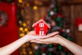 Human hands holding decorative red house against blurred background. Christmas and home comfort concept. Royalty Free Stock Photo