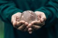 Human hands holding earth sphere crystal or sustainable globe glass with sunlight at green nature background in ecology Royalty Free Stock Photo