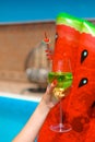 Human Hands Holding Glass. Coctail above watermelon float mattress by swimming pool on villa resort. Summer vacation. Luxury