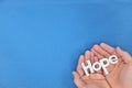 Human hands holding hope word cutout in blue background. Top view with copy space. Royalty Free Stock Photo