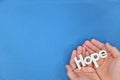 Human hands holding hope word cutout in blue background. Top view with copy space.