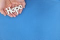 Human hands holding hope word cutout in blue background. Top view with copy space. Royalty Free Stock Photo