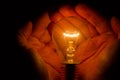 Human hands holding a light bulb to conserve energy darkness Royalty Free Stock Photo