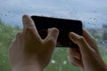 Human hands holding the phone and playing on the touch screen with your thumbs. on the background of green nature and blue sky.