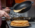 Human hands holding a spatula and a frying pan spread hot pancake on the dish from which steam comes. Home kitchen. Royalty Free Stock Photo
