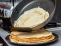 Human hands holding a spatula and a frying pan spread hot pancake on the dish from which steam comes. Home kitchen. Royalty Free Stock Photo