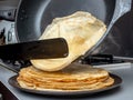 Human hands holding a spatula and a frying pan spread hot pancake on the dish from which steam comes. Home kitchen Royalty Free Stock Photo