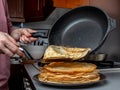 Human hands holding a spatula and a frying pan spread hot pancake on the dish from which steam comes. Home kitchen Royalty Free Stock Photo