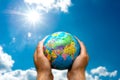 Human hands holds world globe planet earth on blurred blue sky sun and clouds background wallpaper Royalty Free Stock Photo