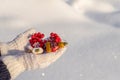 Human hands with open palms in white knitted mittens holding decorative new year toys on fresh snow background in sunny day. Merry