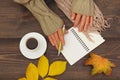 Human hands with a pen and notebook at a wooden table with cup of coffee and autumn leaves and scarf Royalty Free Stock Photo