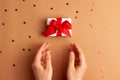 Human hands puts a white paper gift with a red satin ribbon bow on brown background with red stars shapes. Christmas Holidays Royalty Free Stock Photo