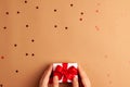 Human hands puts a white paper gift with a red satin ribbon bow on brown background with red stars shapes. Christmas Holidays Royalty Free Stock Photo