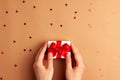 Human hands puts a white paper gift with a red satin ribbon bow on brown background with red stars shapes. Christmas Holidays Royalty Free Stock Photo