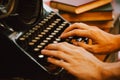 Human hands typing on vintage type writer machine and piles of books on wooden table - very selective focus. Royalty Free Stock Photo