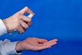 Human hands use spray, disinfectant, antiseptic in bubble, jar on blue background