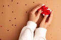 Human hands in white sweater puts a white paper gift with a red satin ribbon bow on right on brown background with red stars Royalty Free Stock Photo