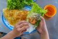 Human hands wrapping Vietnamese shrimp crepe with vegetables- Banh Xeo