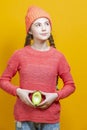 Human Health Concepts. One Teenage Girl In Coral Knitted Clothing With Split Avocado Fruit In Front of Belly as a Demonstration of