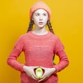 Human Health Concepts. One Teenage Girl In Coral Knitted Clothing With Split Avocado Fruit In Front of Belly as a Demonstration of