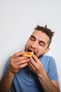 Human holds piece of cheese pizza with tomatoes in his hands and enjoys eating. Young cute Caucasian man with beard and dreadlocks Royalty Free Stock Photo