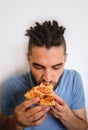 Human holds piece of cheese pizza with tomatoes in his hands and enjoys eating. Young cute Caucasian man with beard and dreadlocks Royalty Free Stock Photo