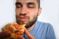 Human holds piece of cheese pizza with tomatoes in his hands and enjoys eating. Young cute Caucasian man with beard and dreadlocks Royalty Free Stock Photo