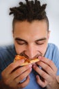 Human holds piece of cheese pizza with tomatoes in his hands and enjoys eating. Young cute Caucasian man with beard and dreadlocks Royalty Free Stock Photo