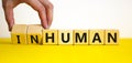 Human or inhuman symbol. Businessman turns wooden cubes and changes the word inhuman to human. Beautiful yellow table white