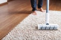 Human legs and a white turbo brush of a cordless vacuum cleaner cleans the carpet in the house Royalty Free Stock Photo