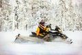 Human in the outfit of a racer in a multi-color jumpsuit and a helmet, driving a snowmobile by the deep snow surface on background