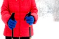 Human in red sport jacket and blue gloves holds two Sticks for hiking