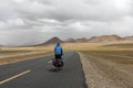 Human riding bicycle on road through desert surrounded by mountains