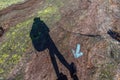 Human shadow walking in wrong direction, against blue arrow on rock