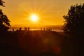 Human silhouettes standing on a hill in front of an orange sunset.