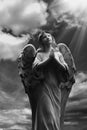 Human soul as angel with wings looking up at the sky in rays of light. Ancient statue. Black and white image