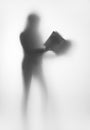 Human standing female body silhouette with book behind a curtain