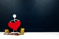 Human stick figure holding a red heart shape with gold coins on side. Cost of healthcare service and health and wealth concept.